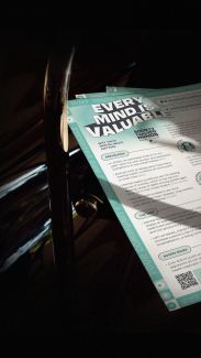 Background image; a printed Society of Valued Minds "Mental Health Multi-Tool" resource sits in the sunlight.