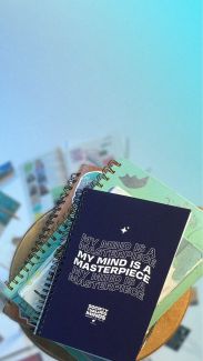 Background image; a stack of Society of Valued Minds journals sit on a stool. The cover of the journal on top reads: "MY MIND IS A MASTERPIECE."